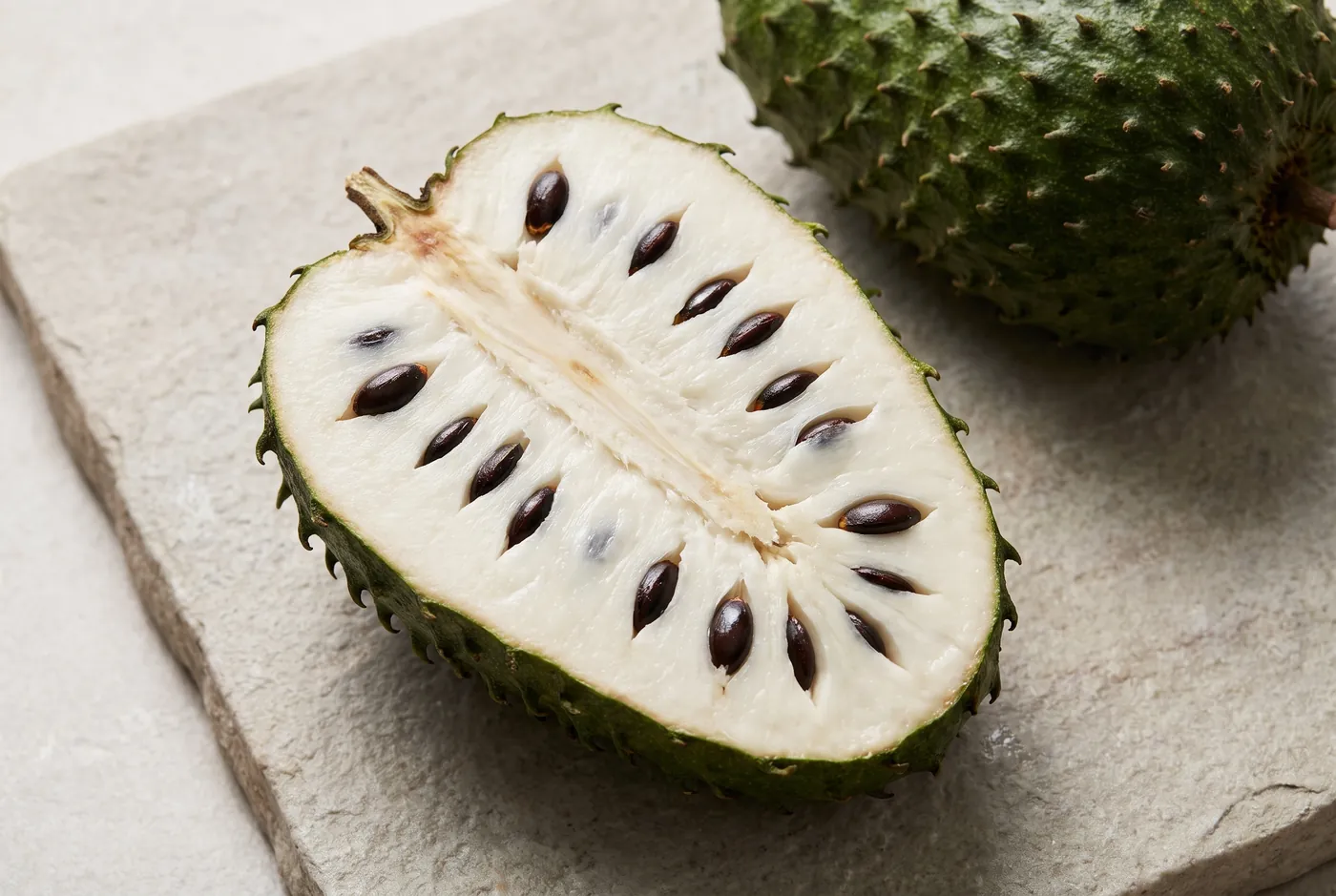 A soursop cut in half lengthwise showing creamy white segmented pulp, a fibrous core and glossy black seeds